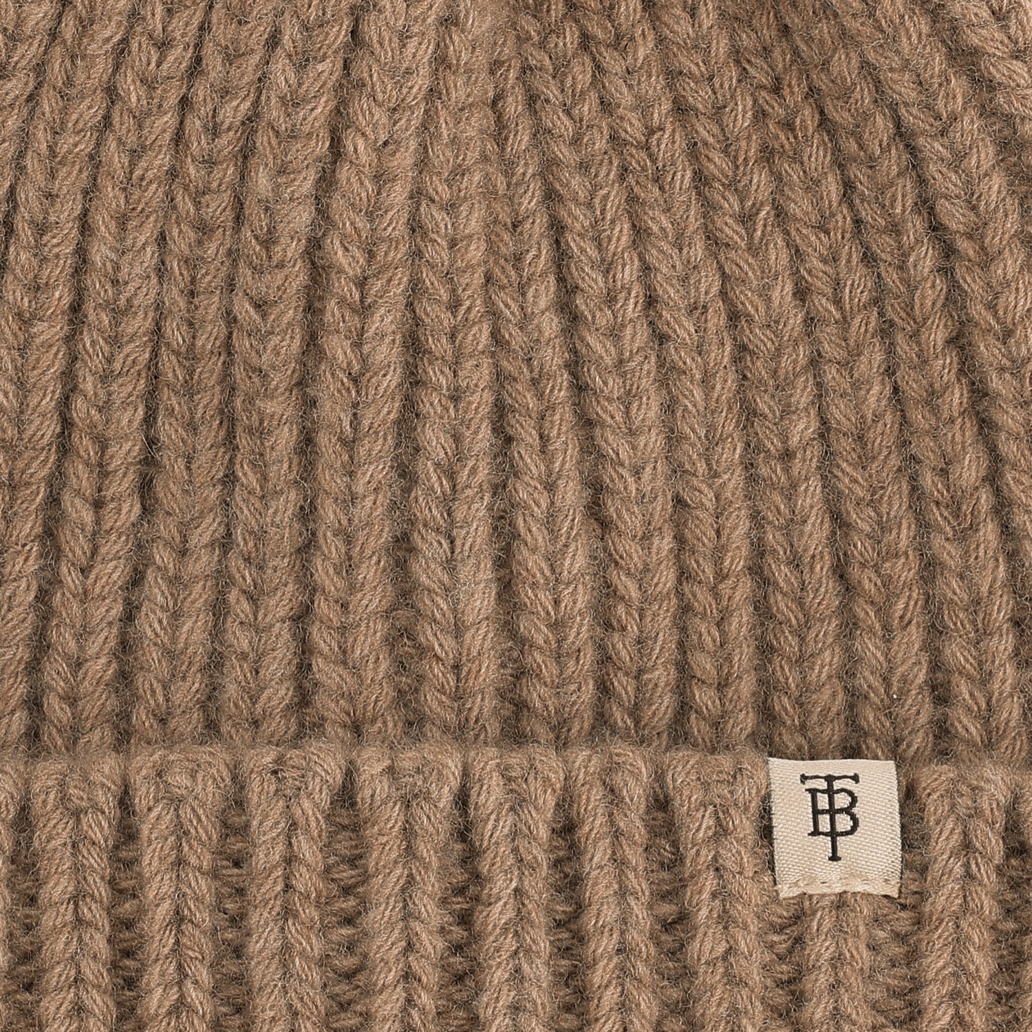 Close-up of the Tom Beckbe Wool Cap, a ribbed brown lambswool beanie with folded brim and small white monogram tag.
