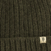 Close-up of Tom Beckbe's Wool Cap in ribbed dark green lambswool with a small beige TB tag.