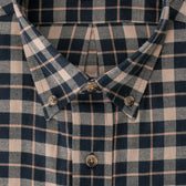 Close-up of a buttoned plaid shirt collar in navy blue and beige with a checkered pattern and brown buttons.