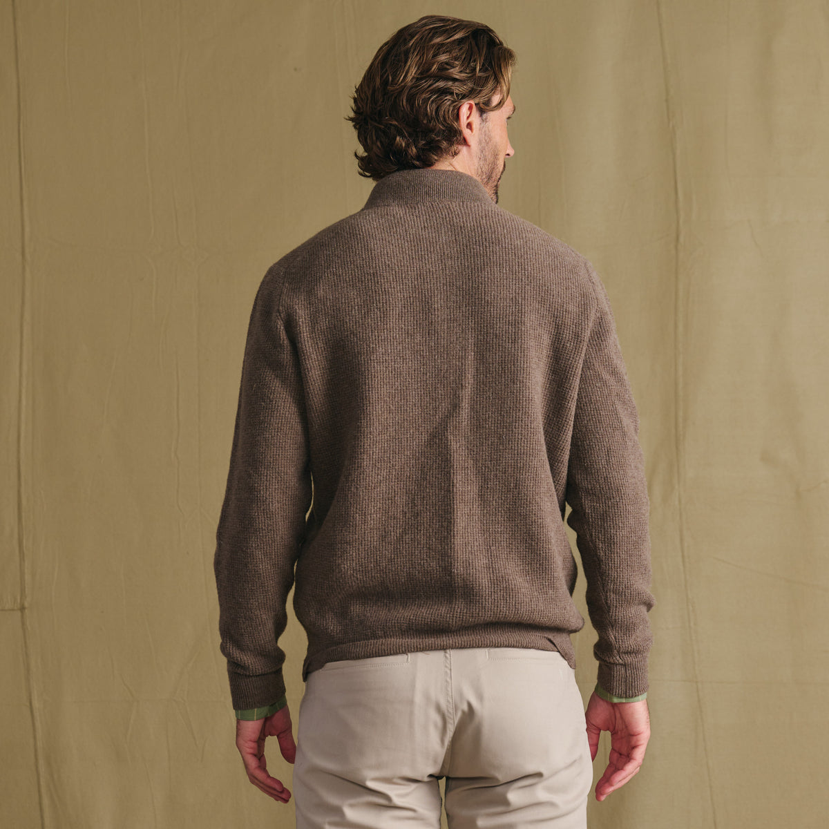 Man in Tom Beckbe Farris Waffle Knit Quarter Zip and light pants stands with back to camera, beige background.