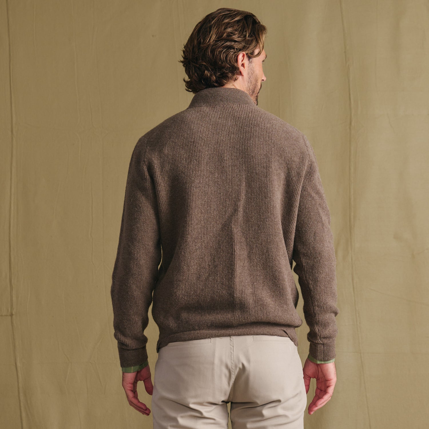 Man in Tom Beckbe Farris Waffle Knit Quarter Zip and light pants stands with back to camera, beige background.