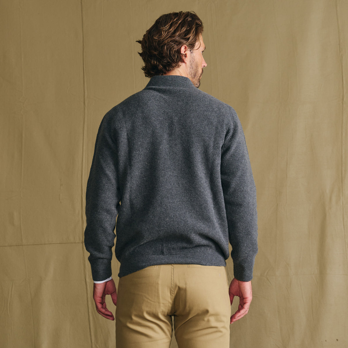 Man facing away in a Tom Beckbe Farris Waffle Knit Quarter Zip and khaki pants, set against a beige background.