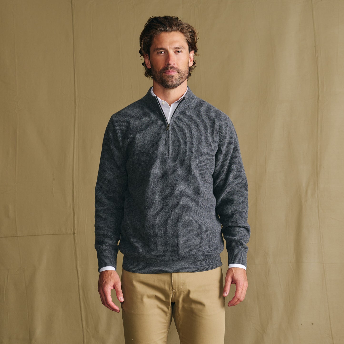 A man models the Tom Beckbe Farris Waffle Knit Quarter Zip in gray with tan pants against a plain tan background.