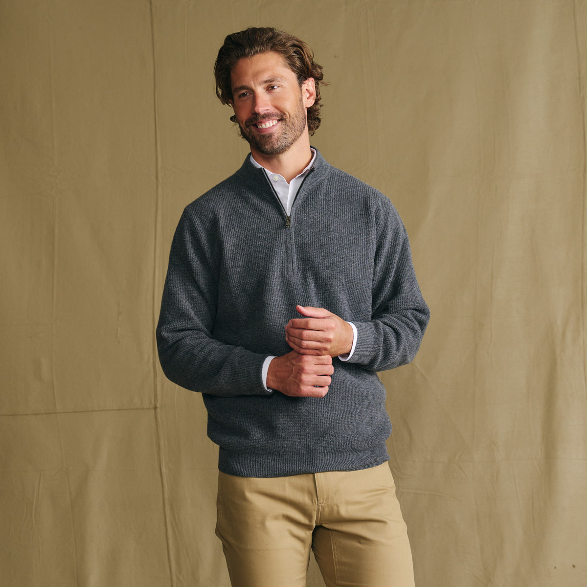 Man wears Tom Beckbe Farris Waffle Knit Quarter Zip and khakis, smiling before a beige backdrop.
