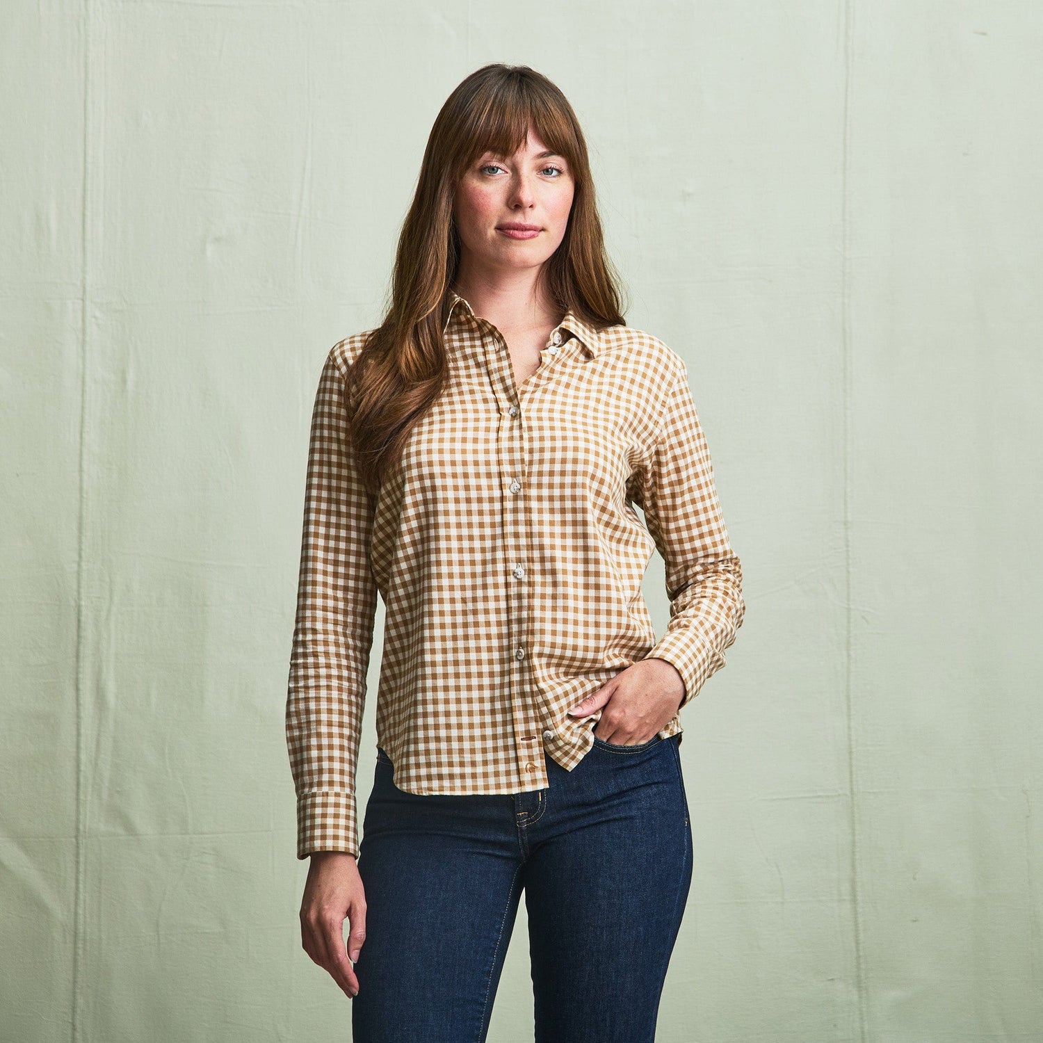 A woman stands against a plain backdrop in a Tom Beckbe Womens Smyth Cotton Twill Shirt and blue jeans.