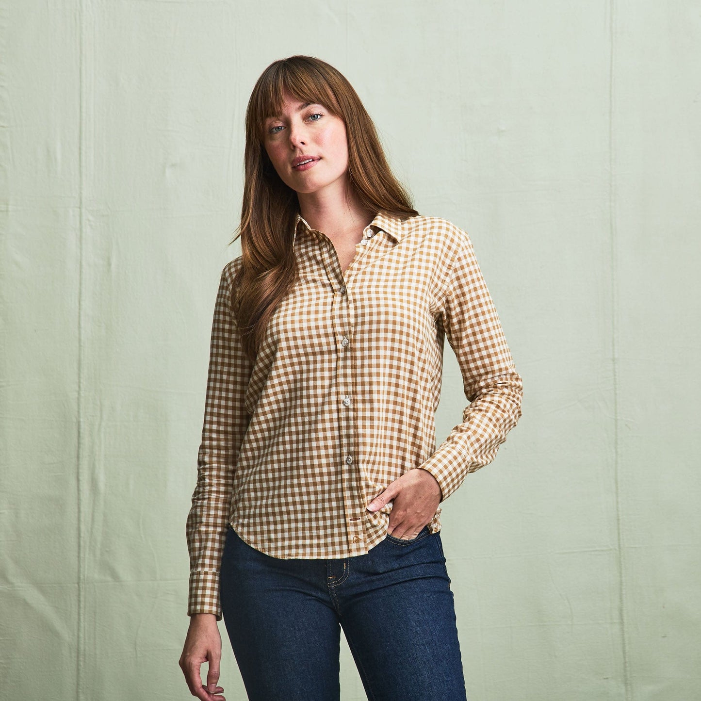 A woman wears the Tom Beckbe Womens Smyth Cotton Twill Shirt with blue jeans, standing against a light green background.