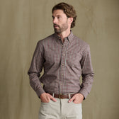 Man wears Tom Beckbe Powell Performance Shirt, UPF 30+, plaid; beige pants; hands in pockets, tan background.