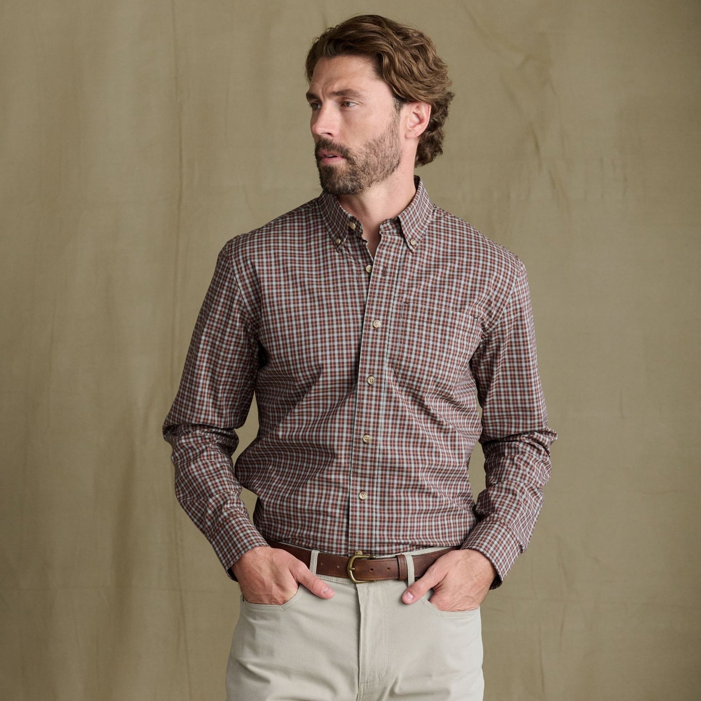Man wears Tom Beckbe Powell Performance Shirt, UPF 30+, plaid; beige pants; hands in pockets, tan background.