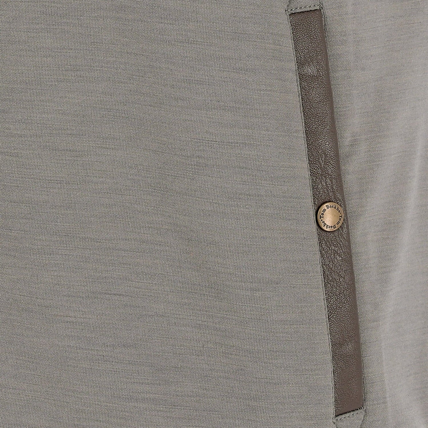 Close-up of a gray fabric garment with a brown vertical trim and a single round metallic button.