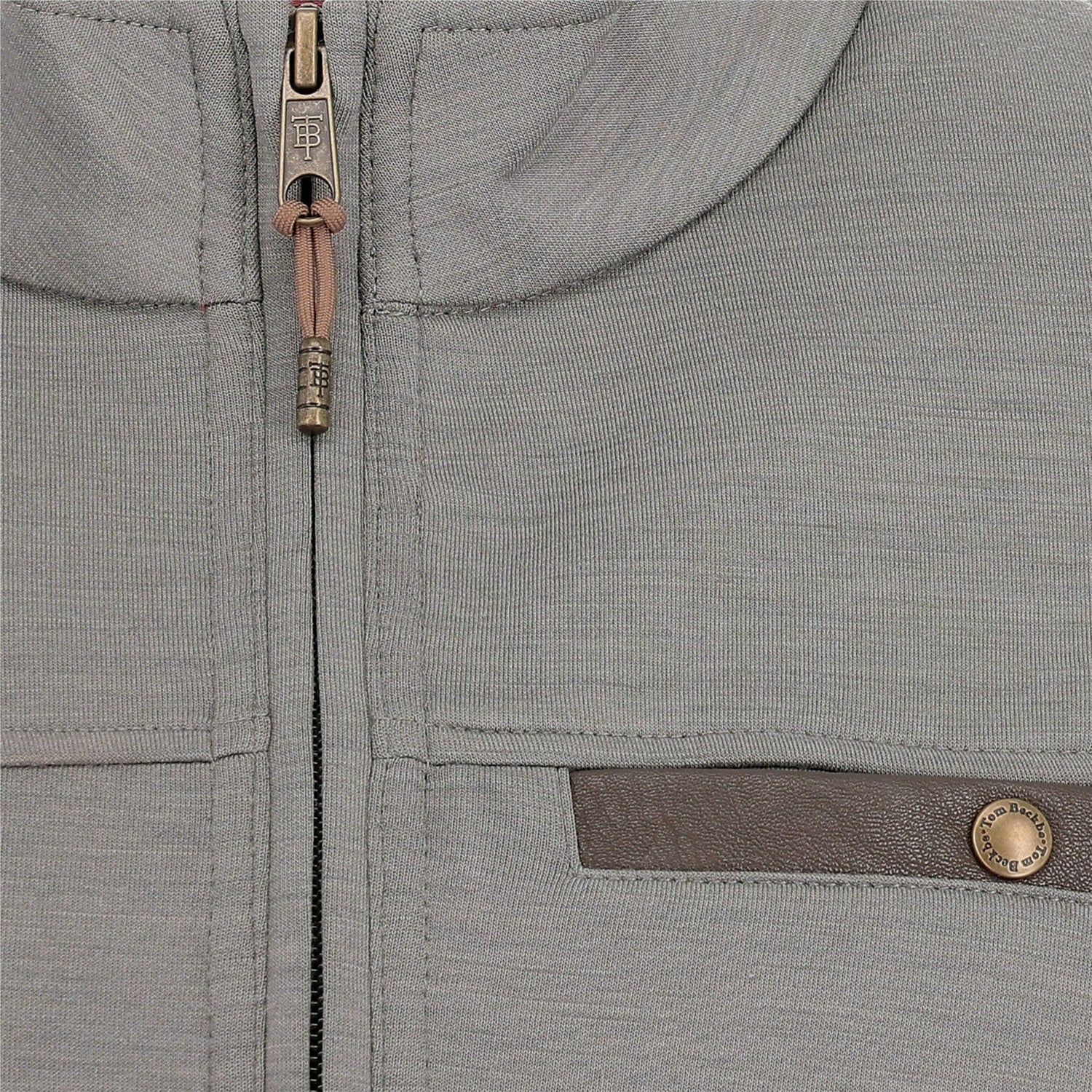 Close-up of a light grey zip-up jacket with a brown horizontal pocket trim and a metallic button detail.