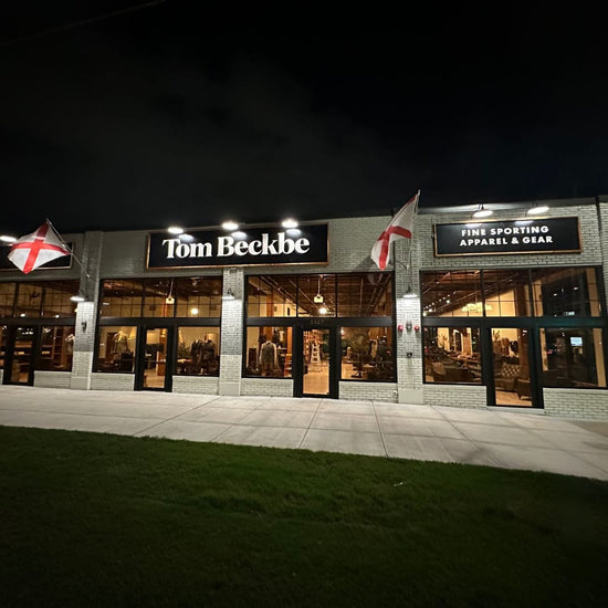 Exterior of a Tom Beckbe store at night with illuminated signs and English flags. Visible interior with sporting apparel displays.