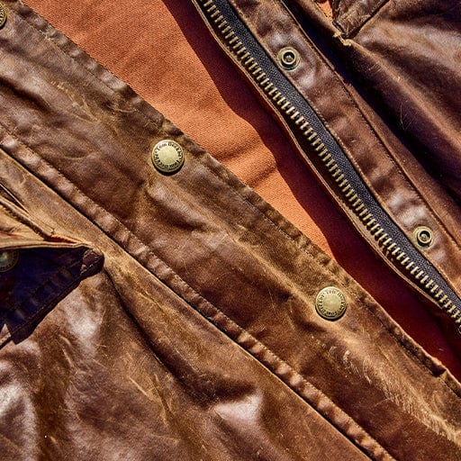 Close-up of a brown leather jacket with metal buttons and a zipper, placed on a rust-colored fabric surface.