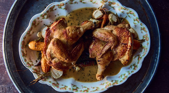 Roasted chicken halves on a floral plate with carrots, garlic, and herbs in a creamy sauce.