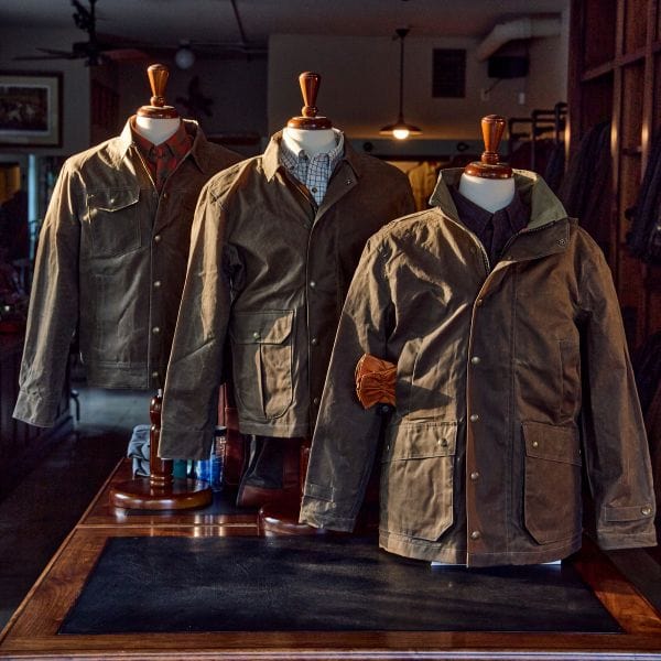 Three brown jackets on display on mannequins in a dimly lit store.