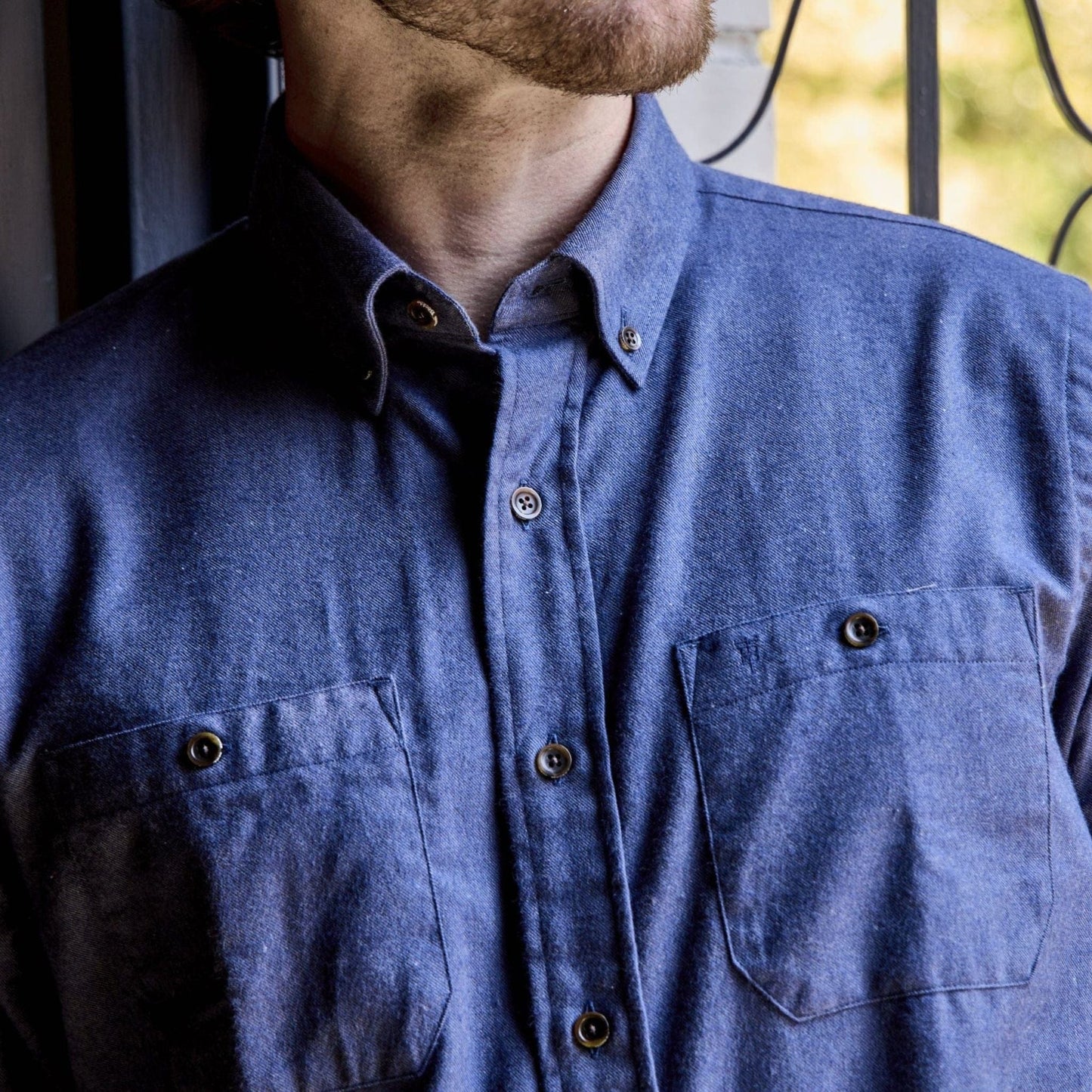 A person wears a Tom Beckbe Dixon Brushed Cotton Twill Shirt with two chest pockets, standing by a window.