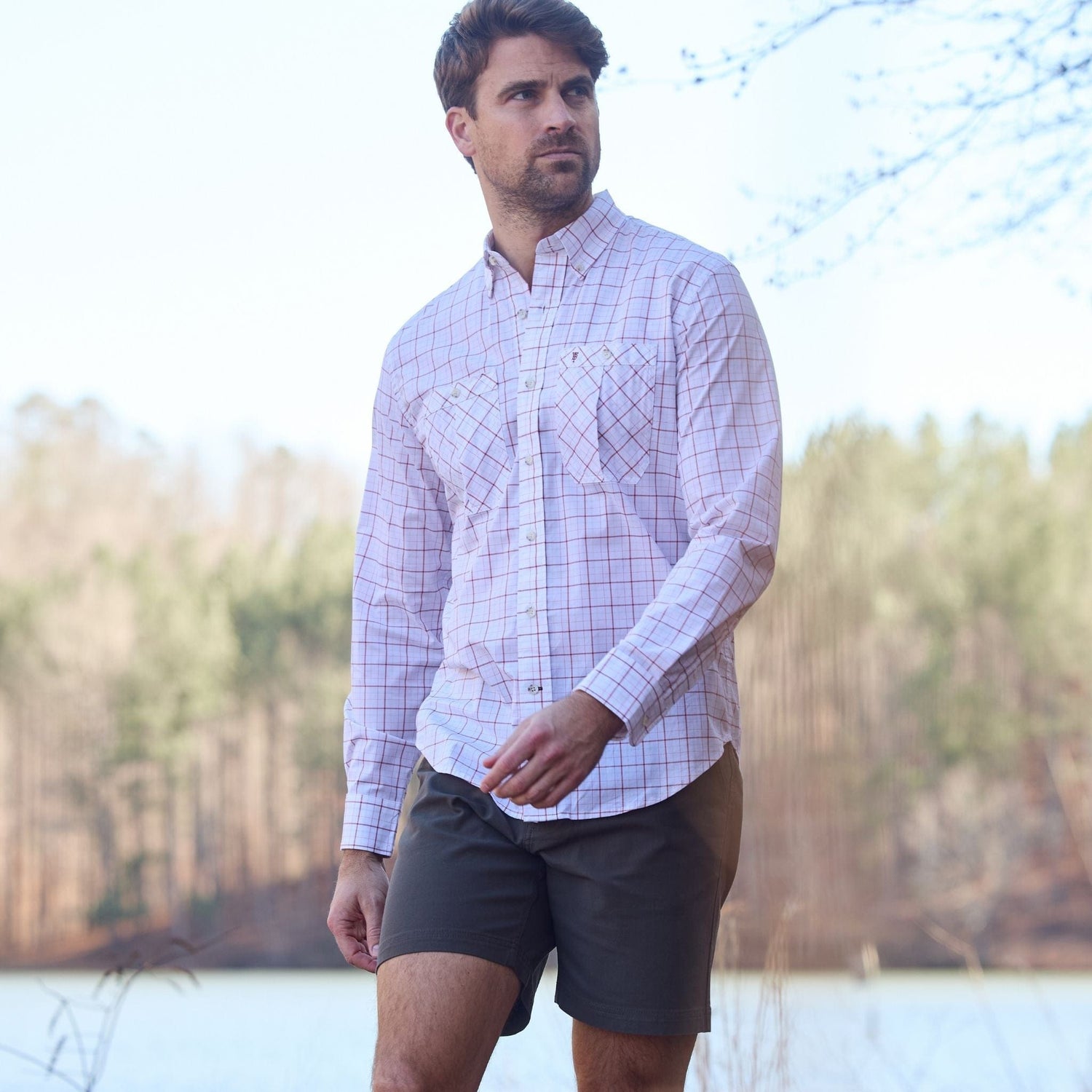 Man in a Tom Beckbe Tidewater Shirt and dark shorts walking near a wooded area.