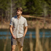 A man in a Tom Beckbe Tidewater short-sleeve shirt stands near a lake with trees in the background.