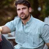Man with short hair and beard wearing a Tom Beckbe Tidewater Shirt, UPF 30+, sits outdoors neutrally.