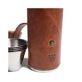 Zoom in of a chestnut leather flask embossed with TB logo and four stainless toasting cups.