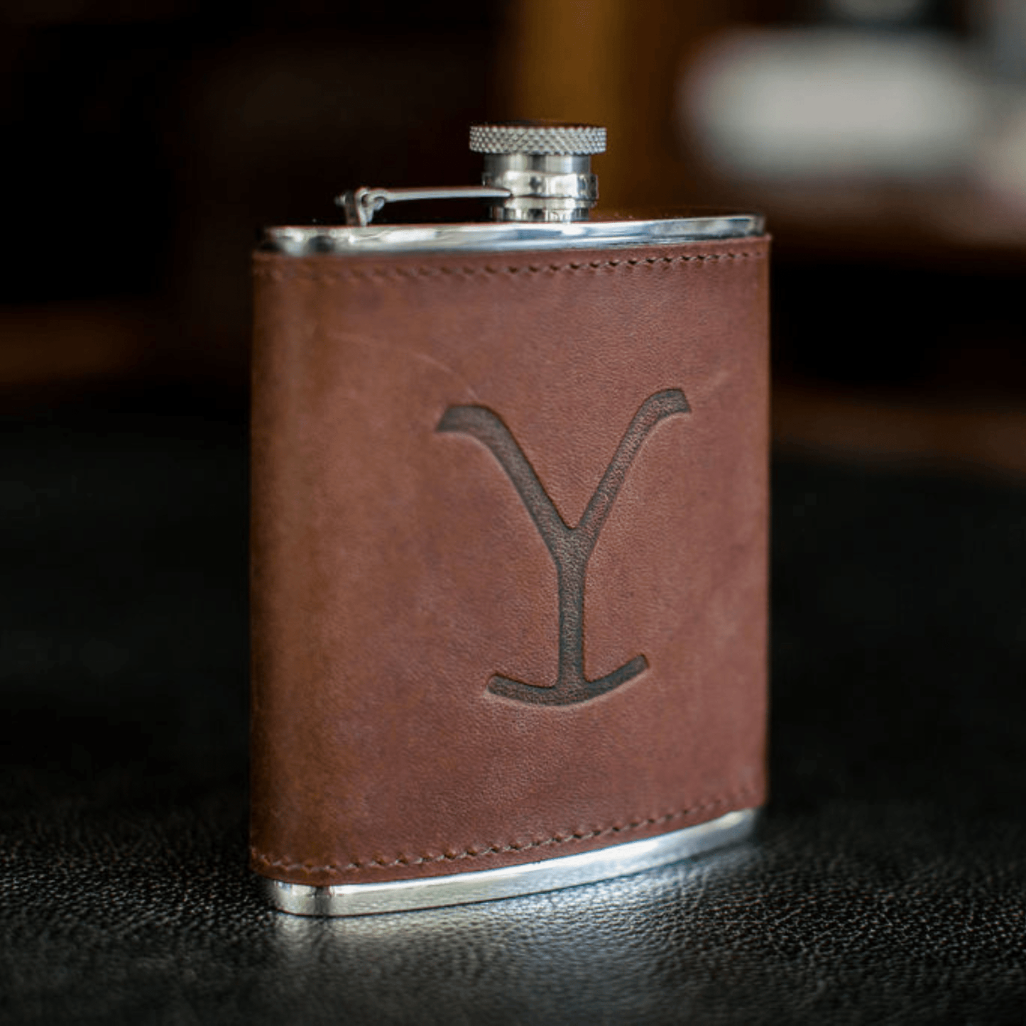 Tom Beckbes Yellowstone Hip Flask, 6oz brown leather with silver, embossed Y, on a black surface.