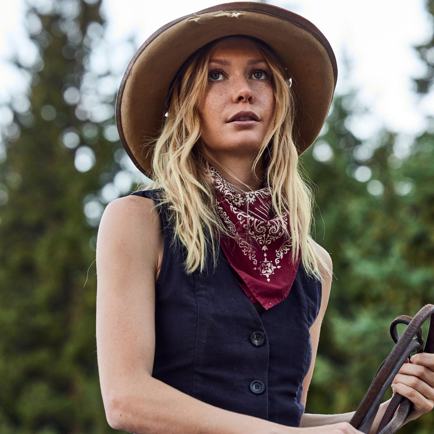 Woman wears a hat and a cotton bandana screen printed with a classic Western American motif in red.