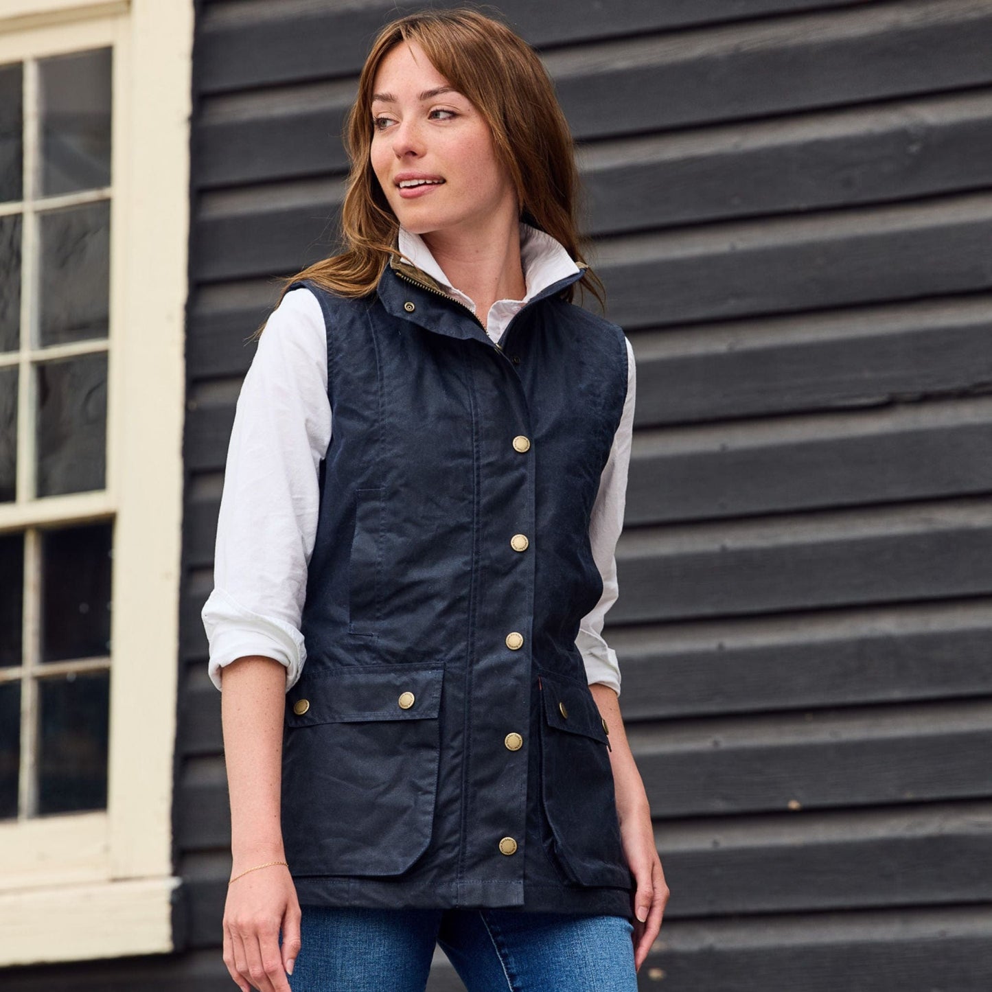 A person in a white shirt and Tom Beckbes Womens Fairmont Vest stands by a dark wooden wall with a window.